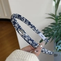 Dettaglio del cerchietto floreale con placca logo argentata e trama in tessuto blu navy - Cerchietto Stretto Blu Notte Floreale