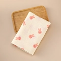 Detail of soft beige muslin swaddle with pink rabbit patterns on a wooden tray - 100x100cm / Pink Rabbit