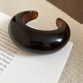 Detail of a dark amber resin open cuff bracelet on a minimalist textured background - Deep Amber (Brown-Round Open)