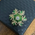 Golden snowflake brooch with emerald green and white zircons on a black jewelry box - Gold Green Brooch
