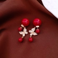 Primer plano de pendientes mariposa bañados en oro 18k con perlas rojas sobre seda - Estilo Perla Roja Bañado en Oro / Rojo
