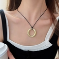 Detail of round golden pendant necklace worn by a model over a black and white top - Gold Round O-Shape with Black Cord