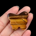 Tiger eye stone butterfly pendant with natural golden-brown stripes held on finger - Tiger's Eye