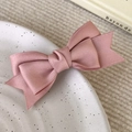 Dettaglio di un fermaglio per capelli a fiocco in raso rosa su un piatto di ceramica lucida - Rosa