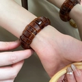 Dettaglio di un bracciale rigido in resina ambrata con motivo tartarugato vintage su un polso - Stile 45 - Caffè Scuro