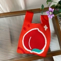 Close-up of red knitted tote bag featuring a peach pattern on a textured glass table - Red Peach