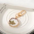 Detail of round resin keychain with irregular gold edge and natural dried green leaf - Leaf