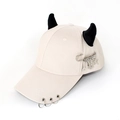 Detail of beige baseball cap featuring black demon horns and punk metal ring accessories - Safety Pin Tools Beige