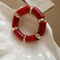 Close-up of red marble-textured acetate beads and gold metal spacers on elastic bracelet - Red