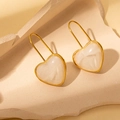 Primer plano de pendientes de corazón de resina con borde dorado sobre base de piedra - Pendientes de Corazón Blanco / Blanco