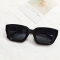 Occhiali da sole squadrati cat-eye neri con montatura spessa su sfondo decorativo - Nero