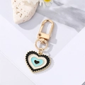 Close-up of enamel heart charm keychain with concentric eye patterns and gold wavy edges - Black Lake Blue Heart Eye