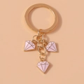 Dettaglio di un portachiavi in metallo dorato con tre ciondoli a forma di diamante rosa - Rosa