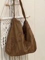 Detail of floral embroidery on a brown suede shoulder bag hanging on a macrame wall - Camel Suede Woven Flower