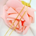 Elegant golden box chain necklace wrapped around a soft pink flower decoration - Box Chain / Gold