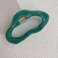 Detail of emerald green wavy hair claw clip with golden metal spring on a white surface - Green