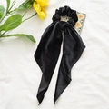 Platte weergave van een zwarte fluwelen scrunchie met linten op witte textuur - Kerst Fluweel Zwart