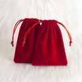 Red velvet drawstring pouch for jewelry storage on a white plush background - Red