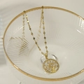 Elegante goldene Halskette mit Lebensbaum-Anhänger und Zirkonia auf einem Glasrand - Gold Weiß