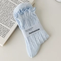 Hellblaue Stricksocken mit Rüschenrand und Zopfmuster auf antikem Buchhintergrund - Hellblauer Zirkon