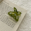 Close-up of a green transparent butterfly hair claw clip resting on an open vintage book - Emerald Green