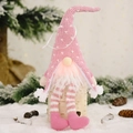 Pink and white glowing Christmas gnome plush with striped long legs on a birch log - Pink