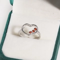 Détail d'une bague coeur en argent avec trois zircons rouges dans son écrin vert - Zircone Rouge Platine