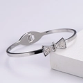 Dettaglio di un bracciale a fiocco argento con zirconi luccicanti su base bianca - Braccialetto a Fiocco / Color Acciaio