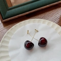 Dettaglio di orecchini a ciliegia bordeaux su un piatto di ceramica bianca e legno - Ciliegia Piccola Rosso Vino