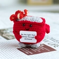 Handmade red crochet crab doll holding a positive quote card for desk decor - Red Dumpster