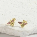 Minimalist gold butterfly stud earrings with pink zircon wings on a white textured stone - Bee