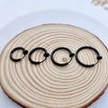 Macro view of four black clip-on hoop earrings in varying sizes on a wooden surface - 2.0mm Wire Diameter 8mm Inner Diameter / Black