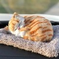 Realistic orange tabby cat plush toy sleeping on a brown cushion in outdoor setting - Large Orange Tabby Cat