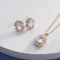 Detail of gold jewelry set with oval halo pendant and matching earrings on blue surface - Gold Oval Clear (HQ0001(8))