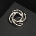 Makroaufnahme der silbernen Knotenbrosche mit detaillierter spiralförmiger Metallstruktur - Silber