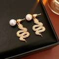 Detalle de pendientes de serpiente dorados con perlas blancas y diamantes en cuero negro - Pendientes de Serpiente con Perla / Dorado