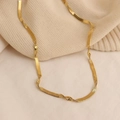 Elegant gold-tone herringbone flat snake chain necklace draped on a beige knit sweater - H1336 Twisted Flat Snake Gold Necklace