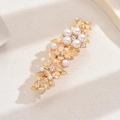Dettaglio del fermaglio per capelli dorato con perle e fiori di strass su sfondo beige - Oro