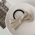 Detailopname van een grote beige strik haarelastiek op een wit rond bord van keramiek. - Wit