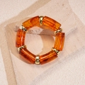 Nahaufnahme des Bernstein-Acryl-Armbands mit goldenen Metallelementen auf Steinplatte - Bernstein