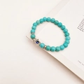 Macro detail of turquoise beaded bracelet with silver Hamsa hand and blue Evil Eye charm - Turquoise