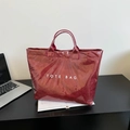 Minimalist burgundy PVC tote bag with white TOTE BAG print on a desk setting - Red