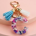 Detalle del llavero letra C de resina con borlas azules y blancas sobre base rosa - Letra C