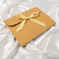 Elegant gold envelope gift box with a yellow ribbon bow on luxury white silk background - Khaki