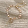 Gros plan d'un bracelet en perles avec breloque marguerite sur tricot doux - Perle d'Eau Douce/Cuivre Plaqué Or/Zircone / Bracelet en Perles d'Eau Douce Fleur en Zircone