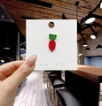 Dettaglio macro della spilla a carota in smalto con bordi dorati su carta - Ravanello Rosso Brillante
