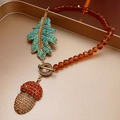 Macro detail of acorn and leaf pendants with rhinestones on an amber bead necklace - Necklace-Brown Pinecone