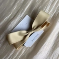 Cream satin 3D bow hair clip on a white card against soft rippled fabric background - Yellow