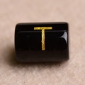 Macro shot of a black cylindrical bead with a golden T letter for jewelry making - Letter T