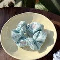 Detailed view of a light blue striped scrunchie with pink ACED embroidery on a beige plate - Pink Edge - Blue Green Stripes % Scrunchie
